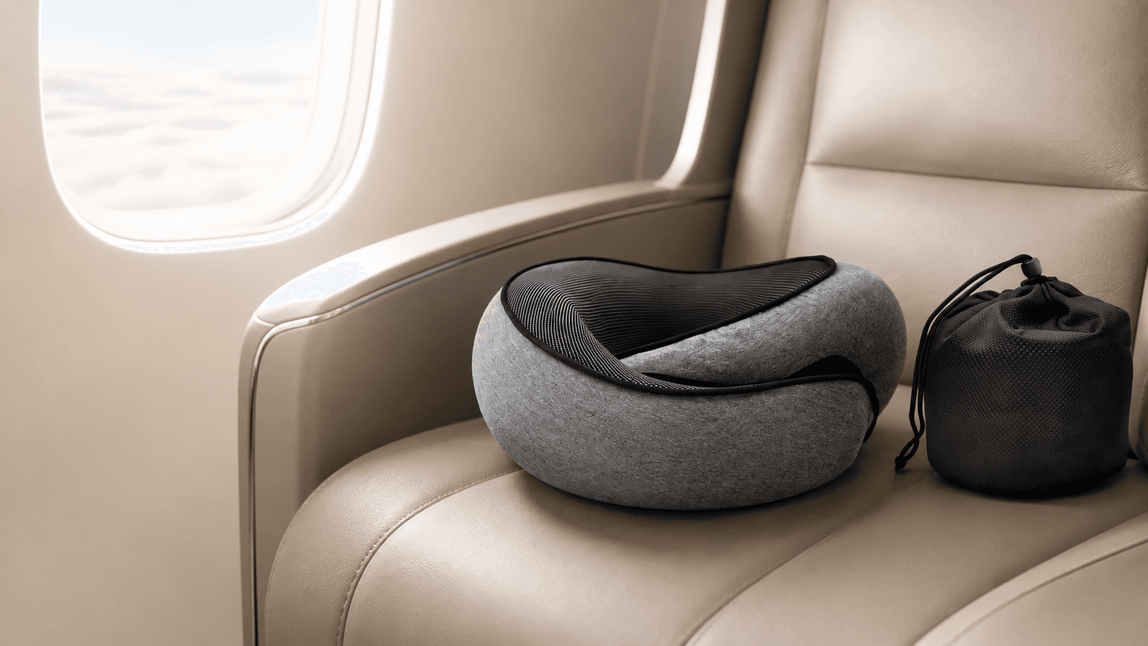 Dodow Pillow posé sur un siège d'avion en cuir beige, avec sa pochette de transport, devant un hublot.